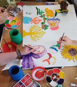 Hands with paintbrushes and pens working on a colourful painting on a table