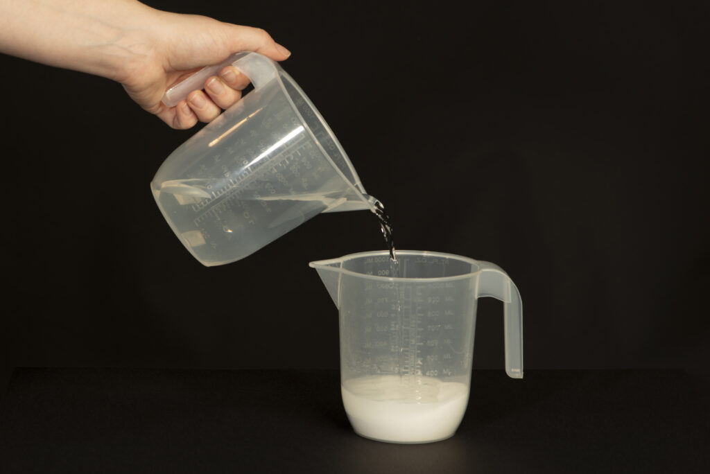 Photograph of someone pouring 1  litre of water into another jug containing sachets A and B.