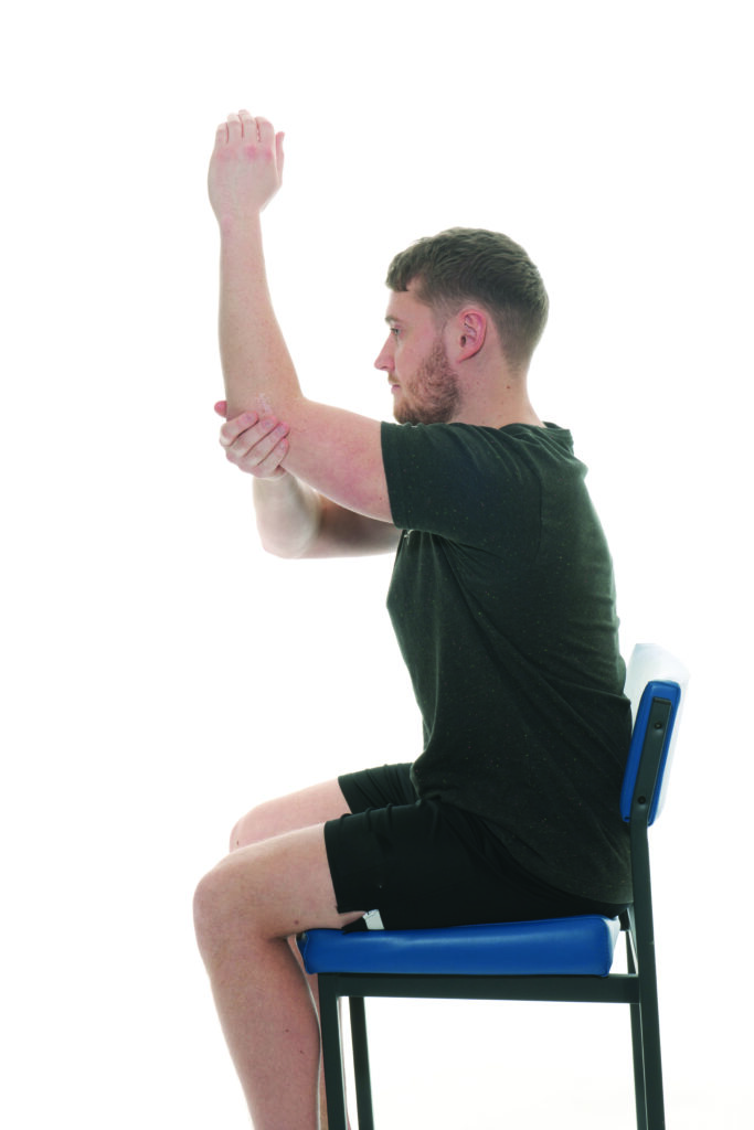 Photograph of a person sat in a chair with their arm raised up in front of them