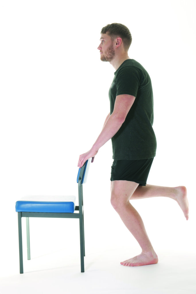 Photograph of a person holding the back of a chair in a squat position with leg bent at the knee