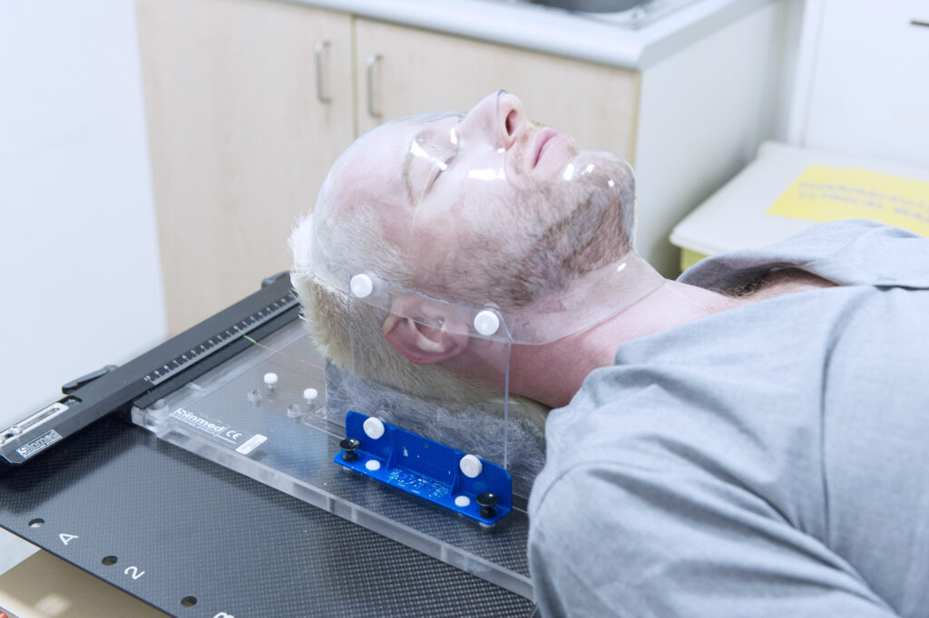 A photograph of a patient with a perspex mask on their face.