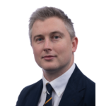 Dr Patrick Gordon headshot. Patrick is wearing a black suit jacket, white shirt and navy tie with yellow and white diagonal lines.