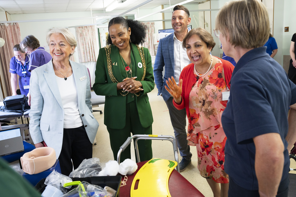 Four smartly dressed people smiling and chatting with healthcare staff in a clinical setting. Medical equipment is displayed in the foreground.