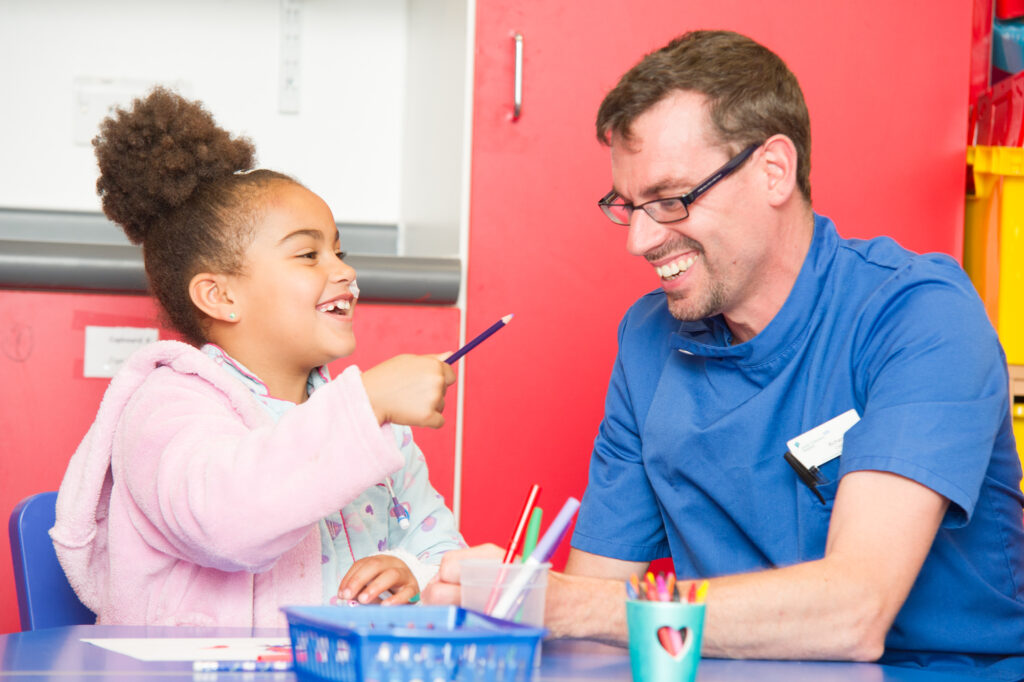 Photograph shows a nurse with a child doing some colouring play