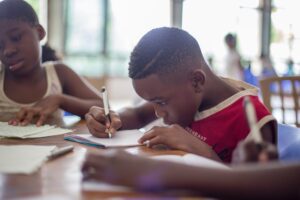 This photograph shows a little boy writing his list of questions in a note book