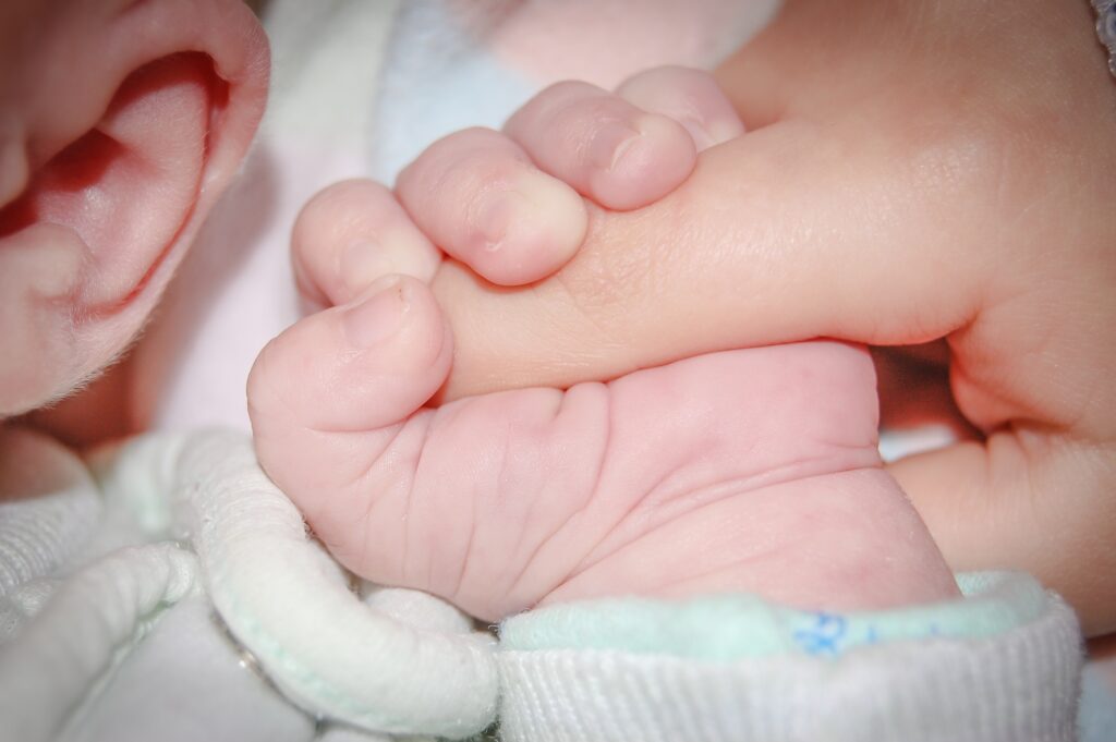 Photograph of a close up of a baby holding an adults finger