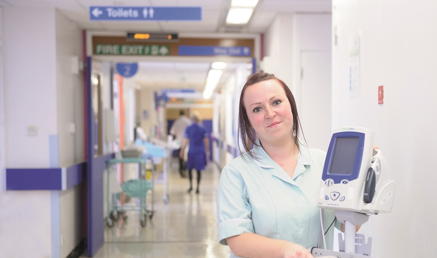 An image showing an Apprentice Clinical Support Worker, which is the 1st step on the Nursing Pathway, in the Leeds Teaching Hospitals NHS Trust on a Ward holding patient healthcare equipment.