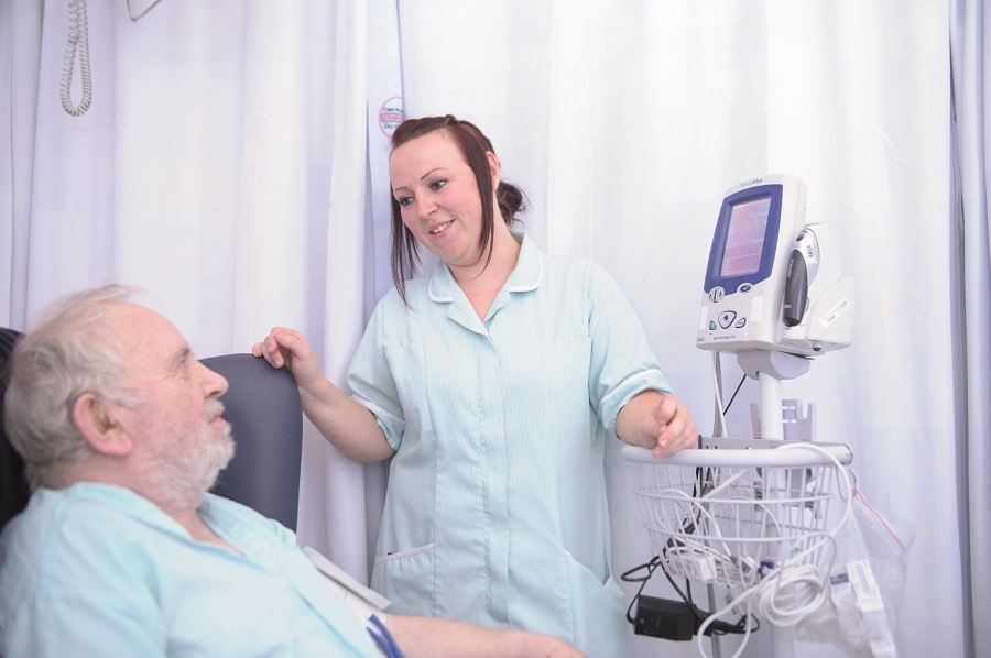 An image showing an Apprentice Clinical Support Worker, which is the 1st step on the Nursing Pathway, in the Leeds Teaching Hospitals NHS Trust assisting a patient in bed.