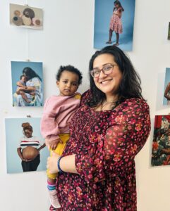 Natalya holding her daughter Zoya stood next to their photo which is on the wall as part of the exhibition.