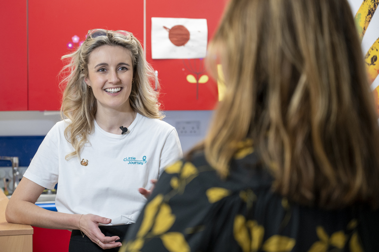 An image of Sophie Copley, Co-Founder of Little Journey, speaking to an interviewer. The interviewer has their back to the camera and the perspective is from over the interviewer's left shoulder.
