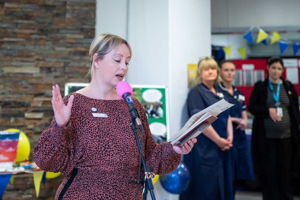 A woman reading from a book into a microphone in front of a crowd