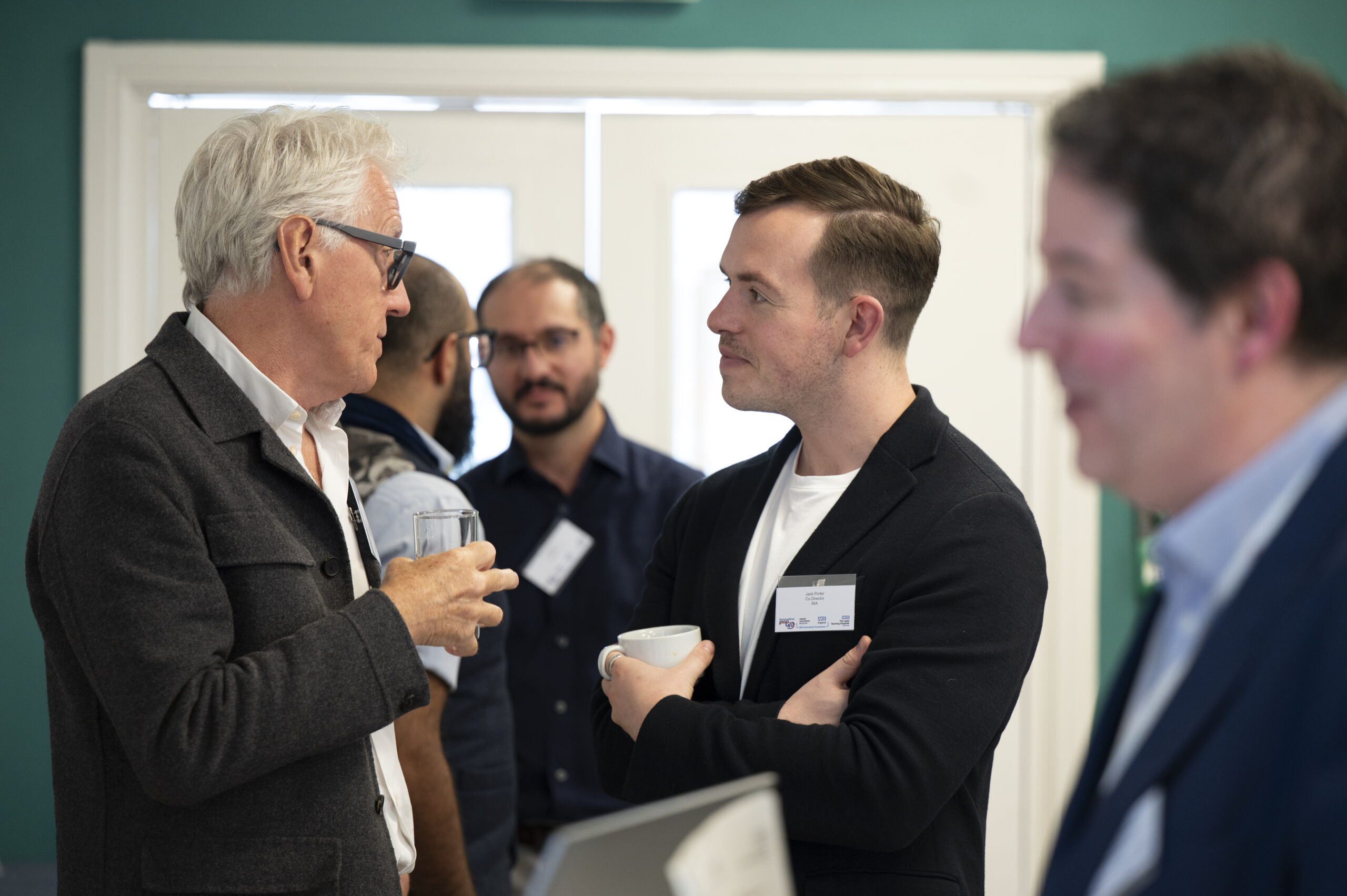 A gallery image of four images, showing clockwise from top left: delegates at the event talking, a speaker presenting to the audience with a Research & Innovation banner behind them, a delegate smiling talking to others, and an image of the audience listening intently to presentations.