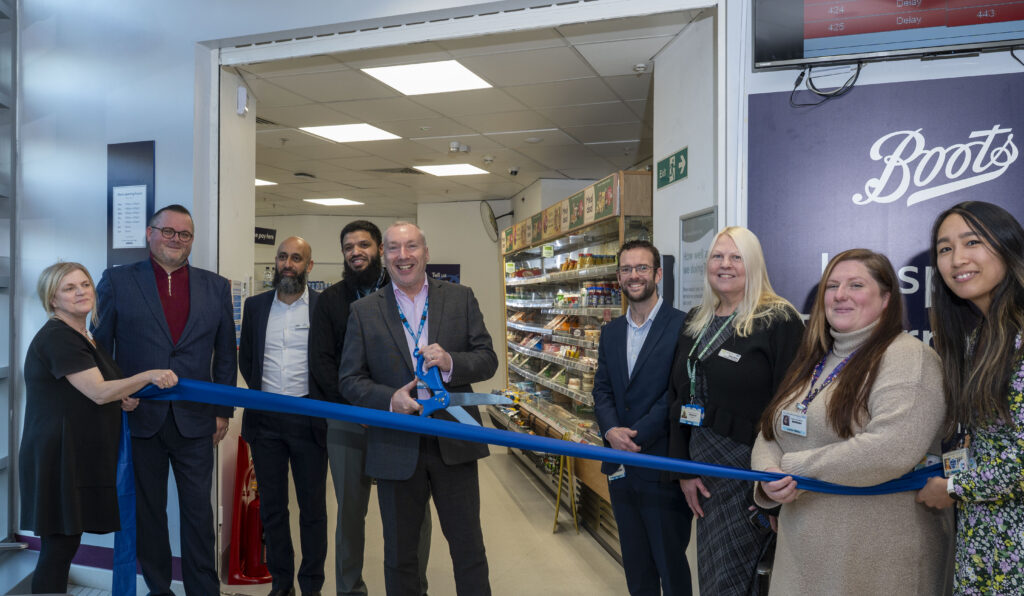A group of people stood outside a Boots pharmacy store holding a blue ribbon. A man in a suit is holding a giant pair of scissors.
