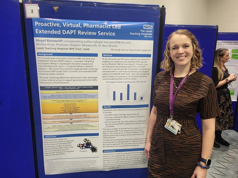 An image of Abi Barrowcliff from the InnoMeds Team standing beside a study poster of the review of extended Dual Antiplatelet Therapy (DAPT) on reducing number of patients taking full dose (DAPT) longer than the recommended and advice on appropriate Infarction Ticagrelor 60mg (extended DAPT).