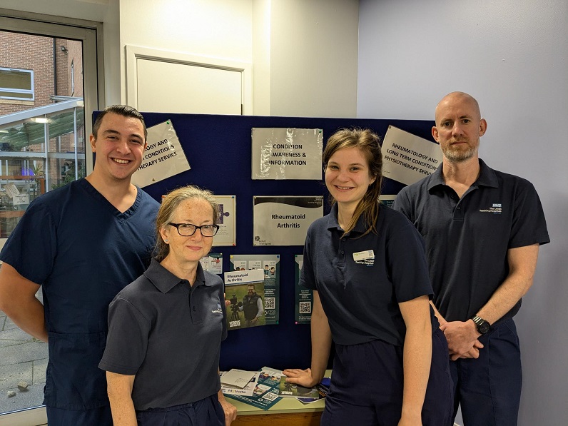 An image taken in 2024 representing the Leeds Teaching Hospitals NHS Trust Rheumatology Service Physiotherapy Team. That contains 2 male and 2 female members of staff standing next to a poster explaining their service.