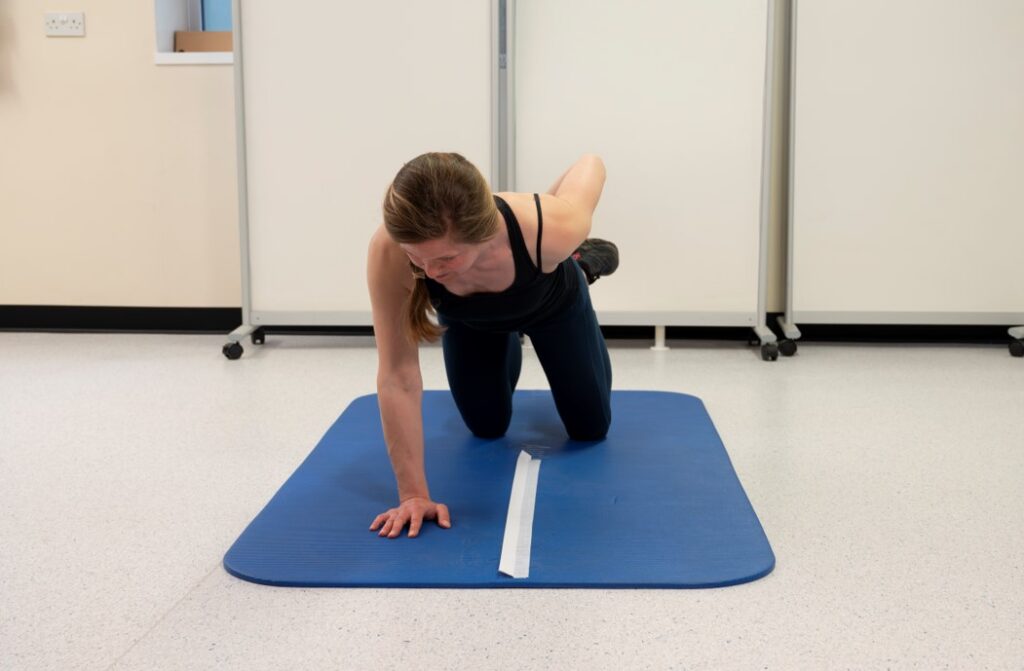 With hips extended, hop the hand over the tape (B) and back (C) to perform one repetition.