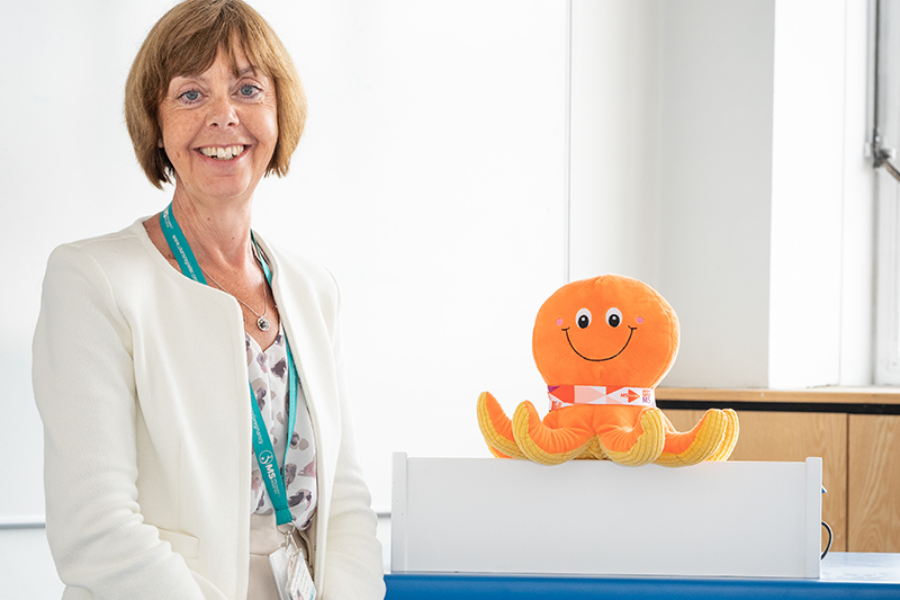Dr Helen Ford standing with an orange octopus soft toy mascot and a white podium with LTHT's logo on the front.