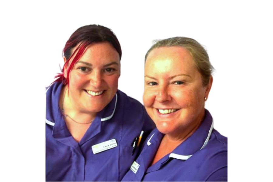 Two midwives in purple uniforms stood next to each other smiling.