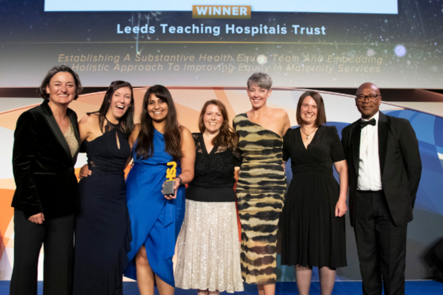 8 people stood on a stage at the HSJ awards celebrating their win.