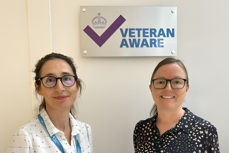 Two females in front of a Veteran Aware plaque that displays a purple check mark
