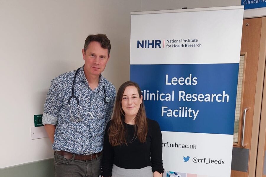 A picture of Dr Klaus Witte and Dr Maria Paton stood next to each other in front of a banner for the Leeds Clinical Research Facility.