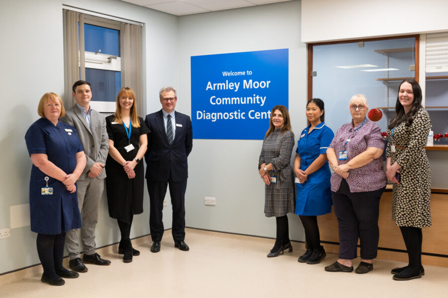 Group of people including Leeds Teaching Hospitals chief executive Phil Wood, standing in front of a blue sign which says "Welcome to Armley Moor Community Diagnostic Centre"