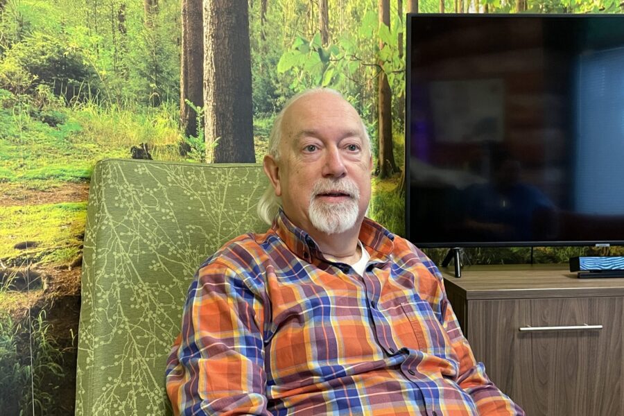 Dr John Roberts, a living donor, sitting in a hospital room, with pictures of a forest behind him