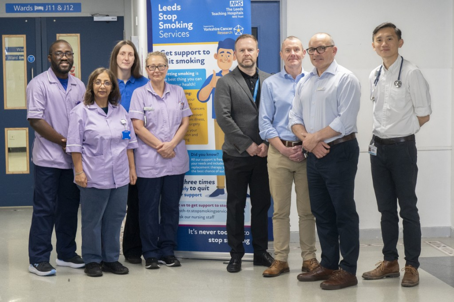 Group of people, half dressed in clinical uniforms, standing in front of a banner promoting stop smoking services.