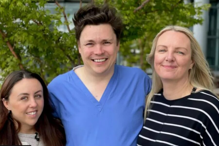 Man in blue scrubs is pictured in centre with two patients on either side of him smiling