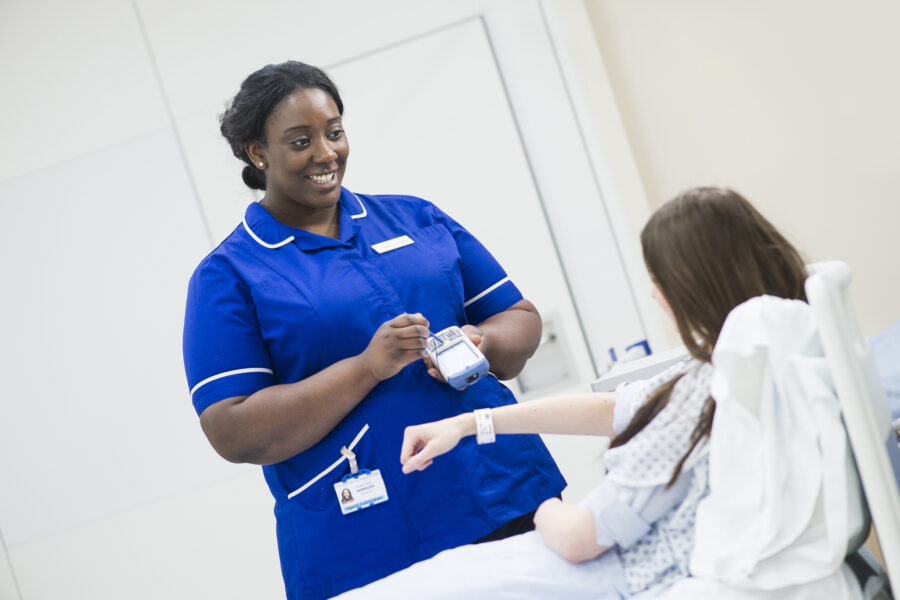 A woman in a blue uniform records information from a young patient in bed