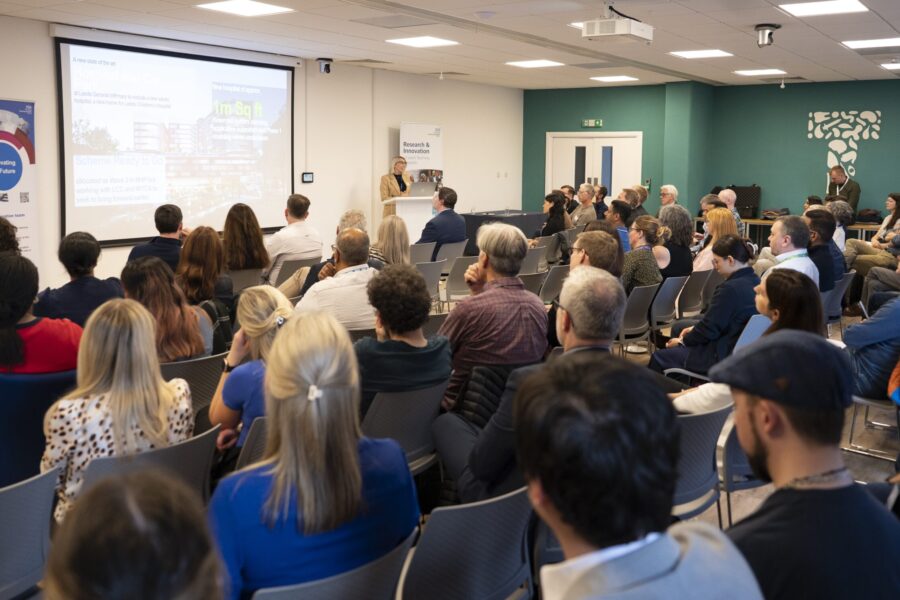 An image showing the audience listening to a speaker presenting with slides.