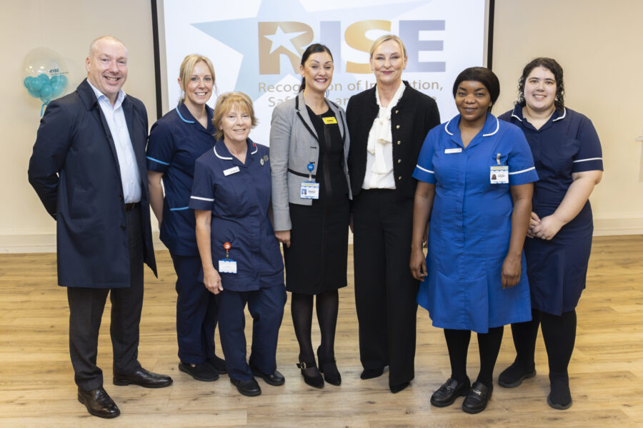 Group of nursing colleagues and executives in front of a banner with the "RISE" logo on it.