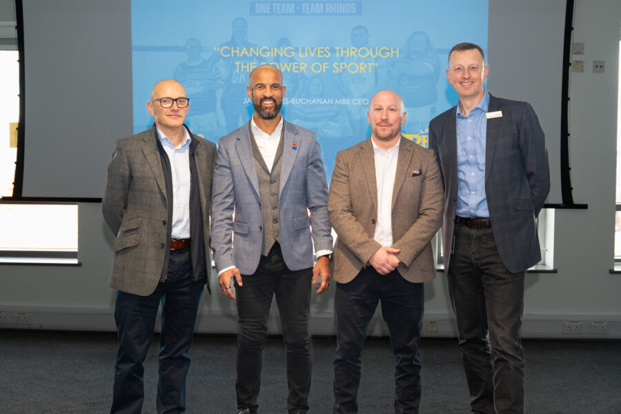 Four men in suits stood in front of a blue display screen