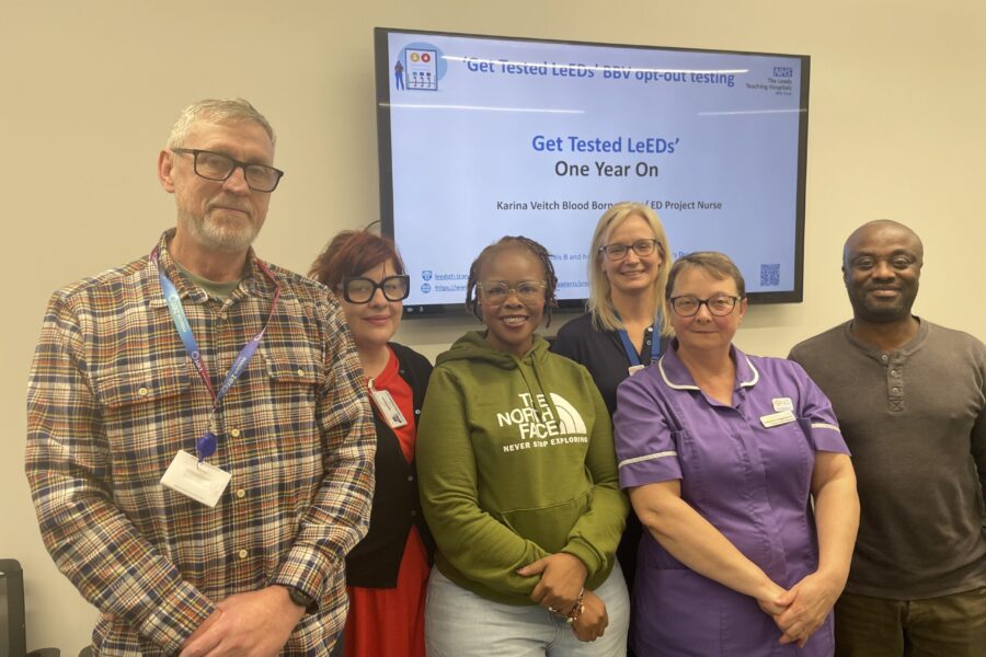 Six people standing in front of a screen with writing on. The writing says "Get Tested Leeds"